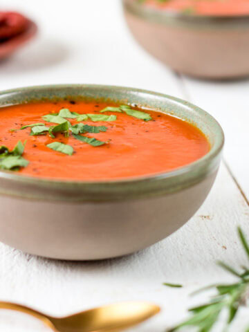 Schüssel mit Tomatensuppe und frischen Kräutern.